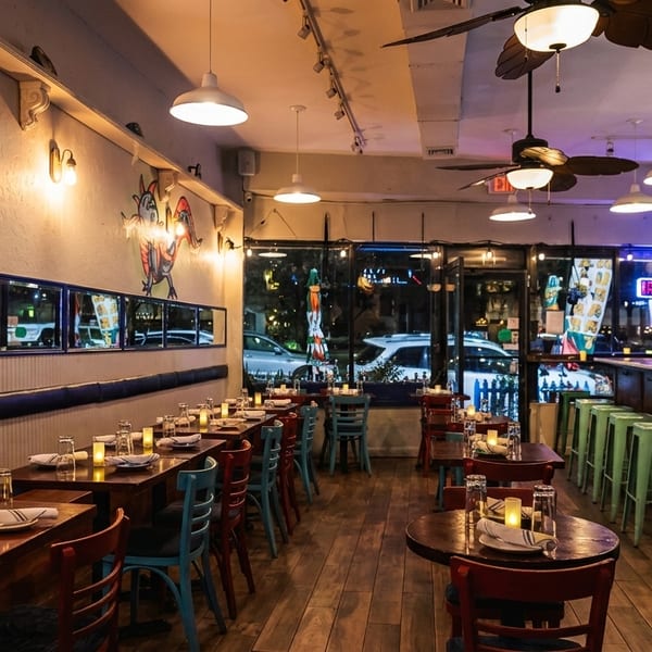 Cozy restaurant interior with wooden tables, colorful chairs, wall murals, and a bar area.