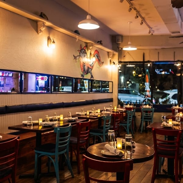 Cozy restaurant interior with wooden tables, colorful chairs, a bar, and a dragon mural on the wall.