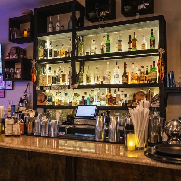 A well-stocked bar with liquor bottles, bar tools, a TV, and a computer screen.