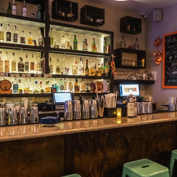 A vibrant bar with a fully stocked liquor shelf, cocktail shakers, and a colorful hummingbird mural.